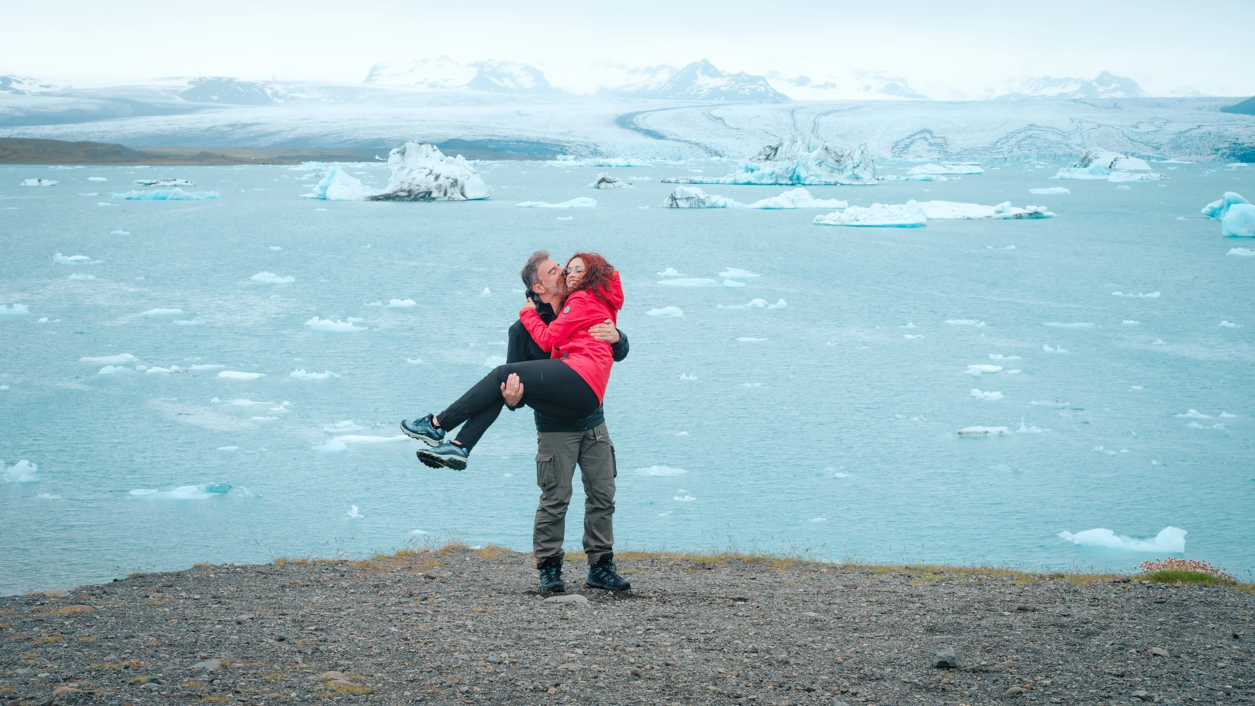 Casal junto à lagoa glaciar Jökulsárlón, rodeado por icebergs na Islândia.