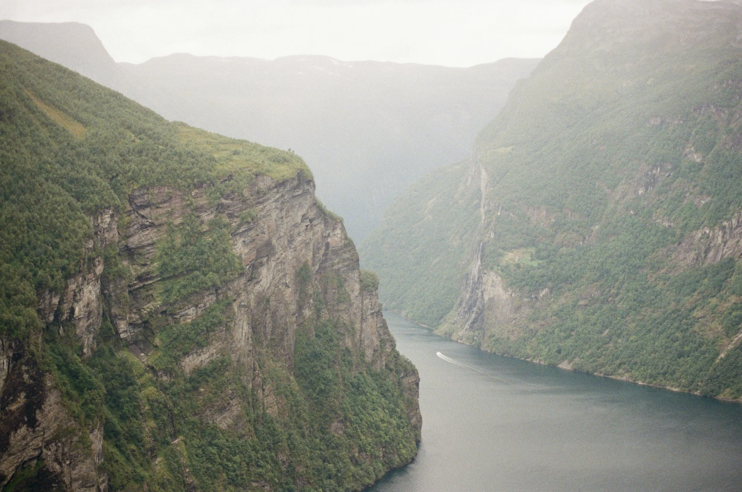 Pequena embarcação privada a navegar num fiorde norueguês entre montanhas íngremes, transmitindo uma experiência exclusiva e tranquila.