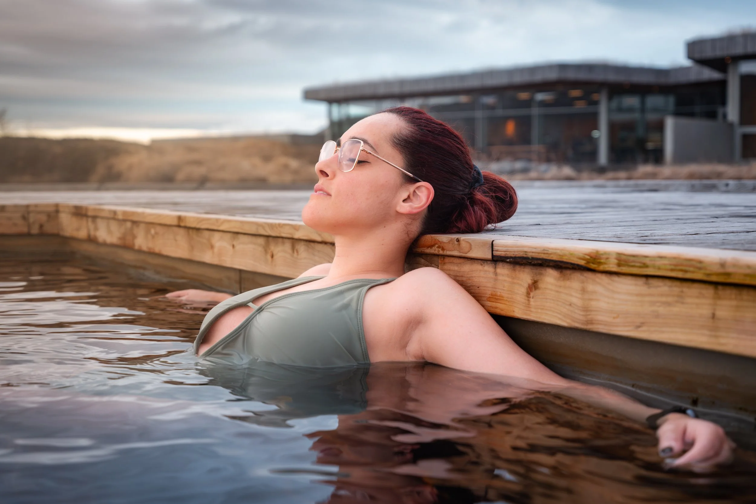 Mulher a relaxar em águas termais exteriores, junto a um alojamento spa, num ambiente calmo e acolhedor na Islândia.