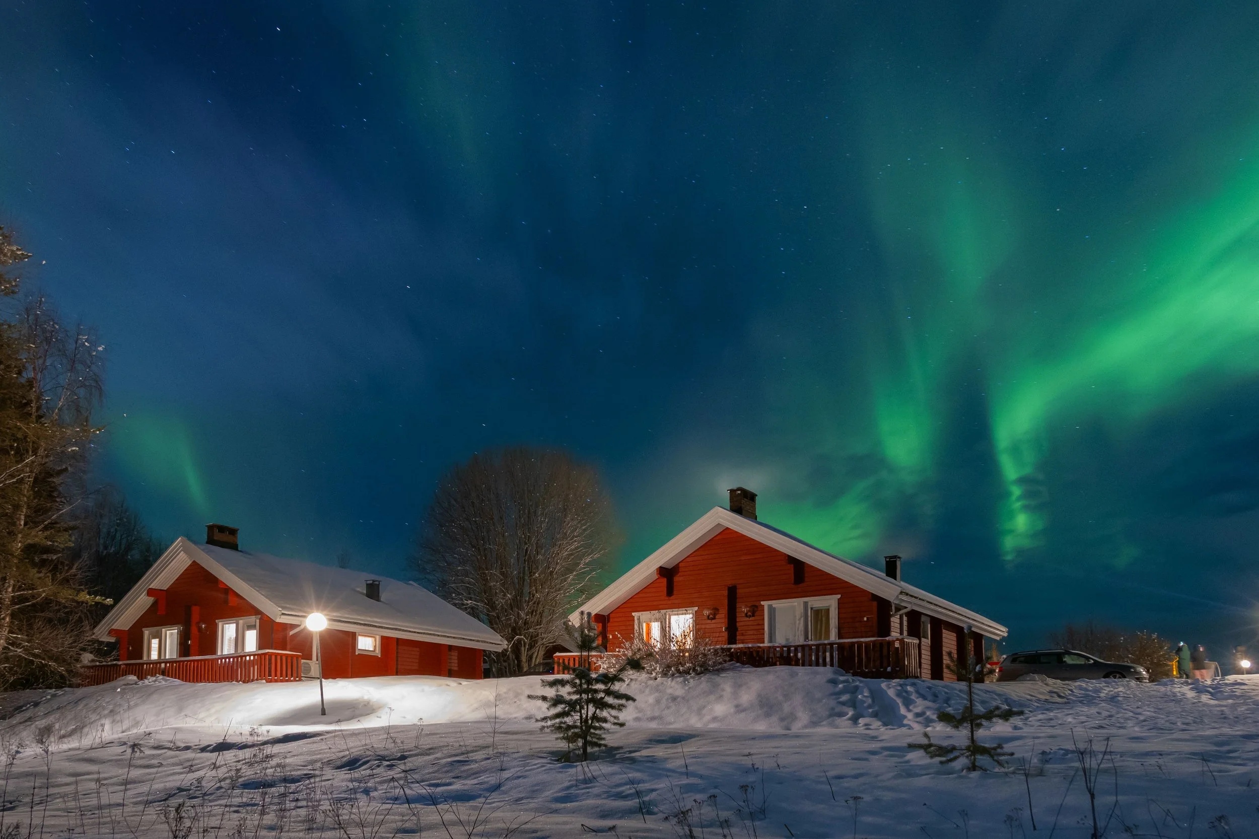 Cabanas de madeira na neve sob a aurora boreal, numa paisagem de inverno na Finlândia.