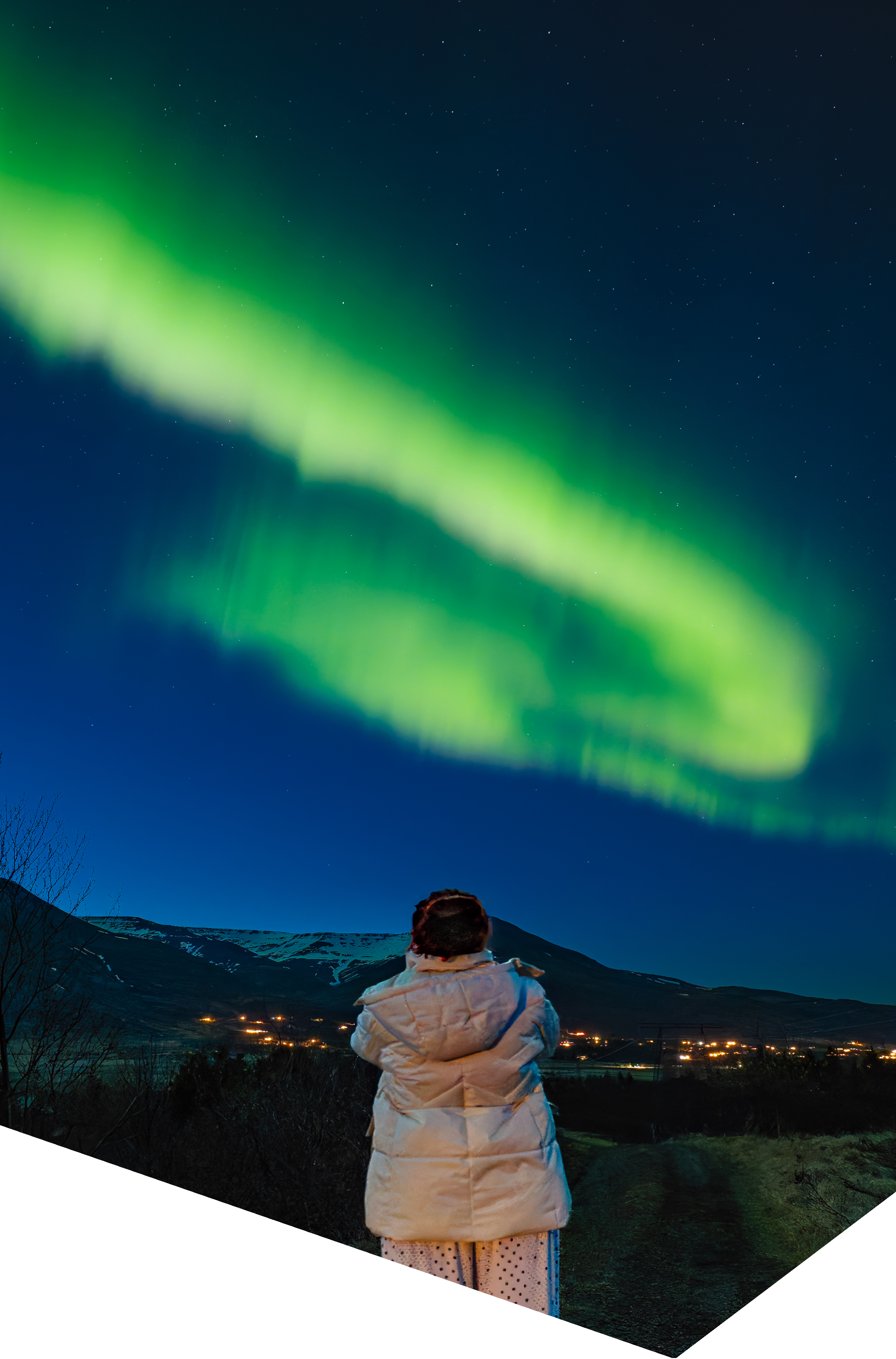 Pessoa a observar uma aurora boreal verde sobre uma paisagem montanhosa durante uma noite nórdica.