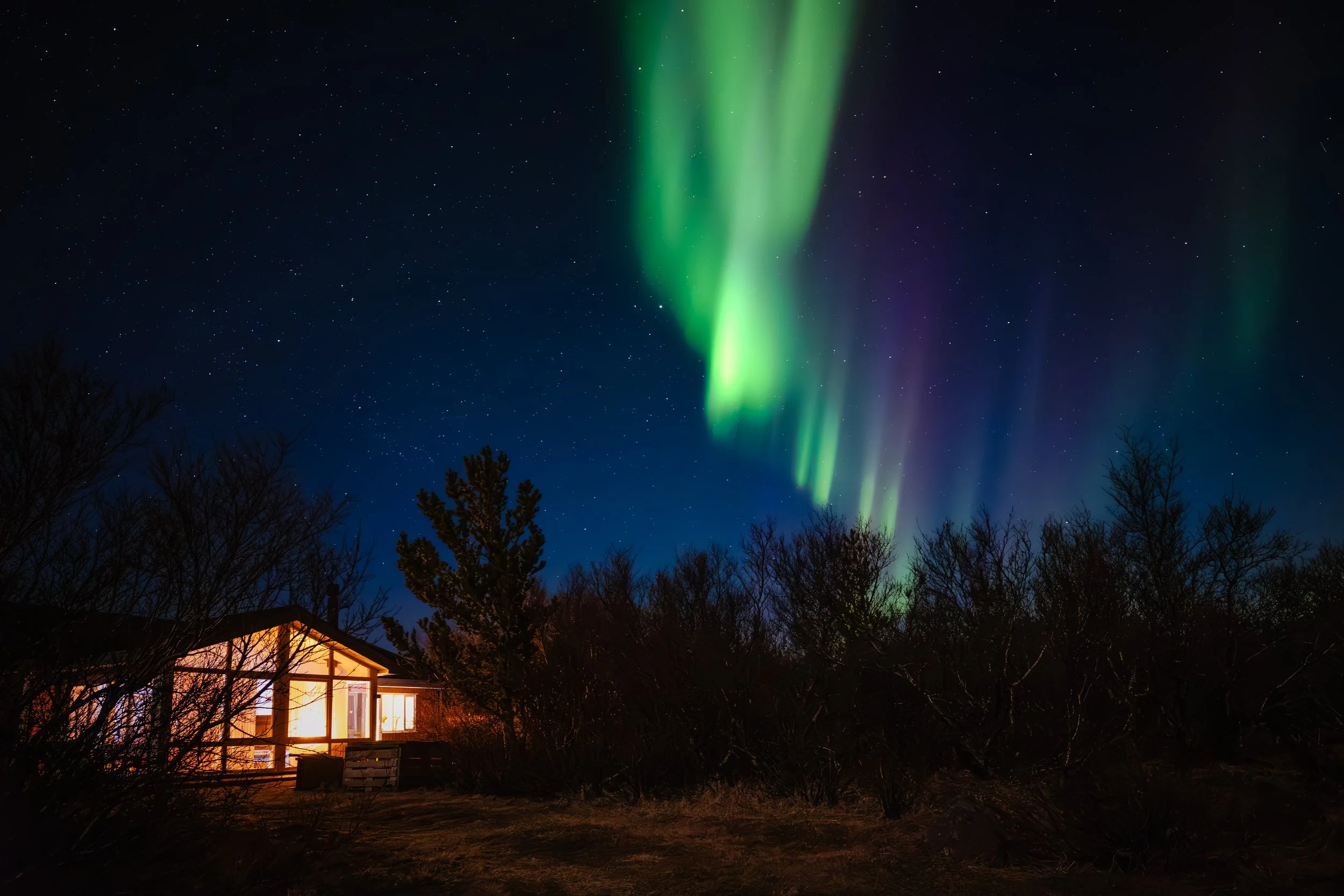 Alojamento nórdico iluminado durante a noite sob uma aurora boreal verde e roxa num céu estrelado.