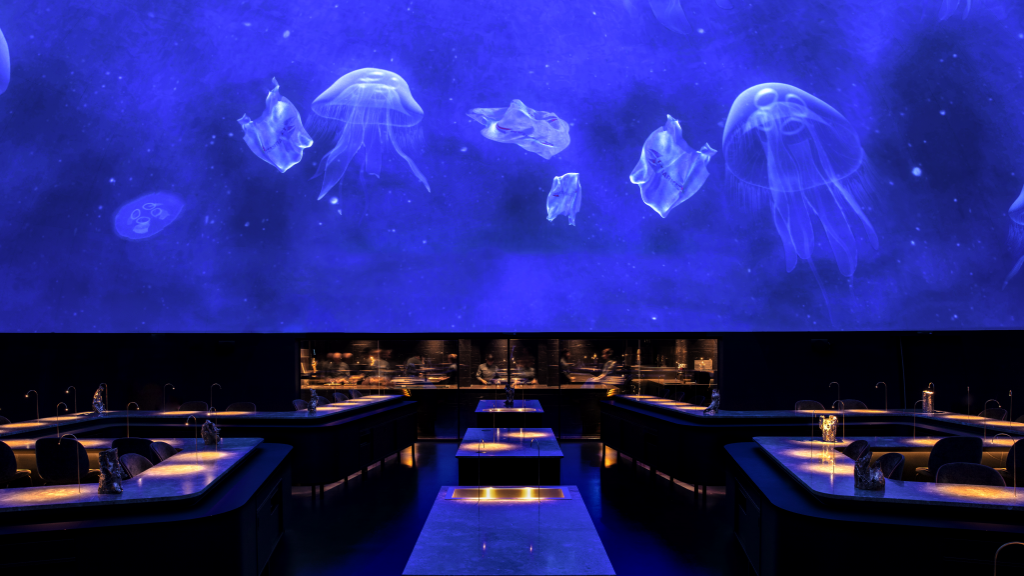 Interior de restaurante Michelin em Copenhaga, com iluminação azul e medusas suspensas sobre a sala de jantar.