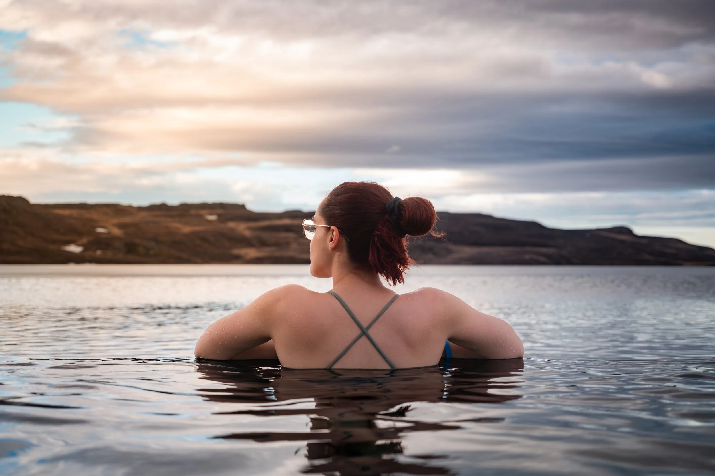 Mulher a relaxar numa piscina geotermal rodeada pela paisagem natural da Islândia.