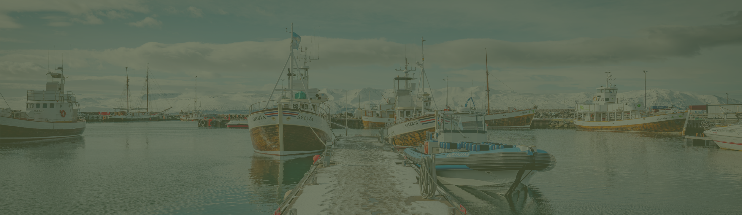 Barcos atracados no porto de Húsavík, no norte da Islândia, com montanhas cobertas de neve ao fundo.