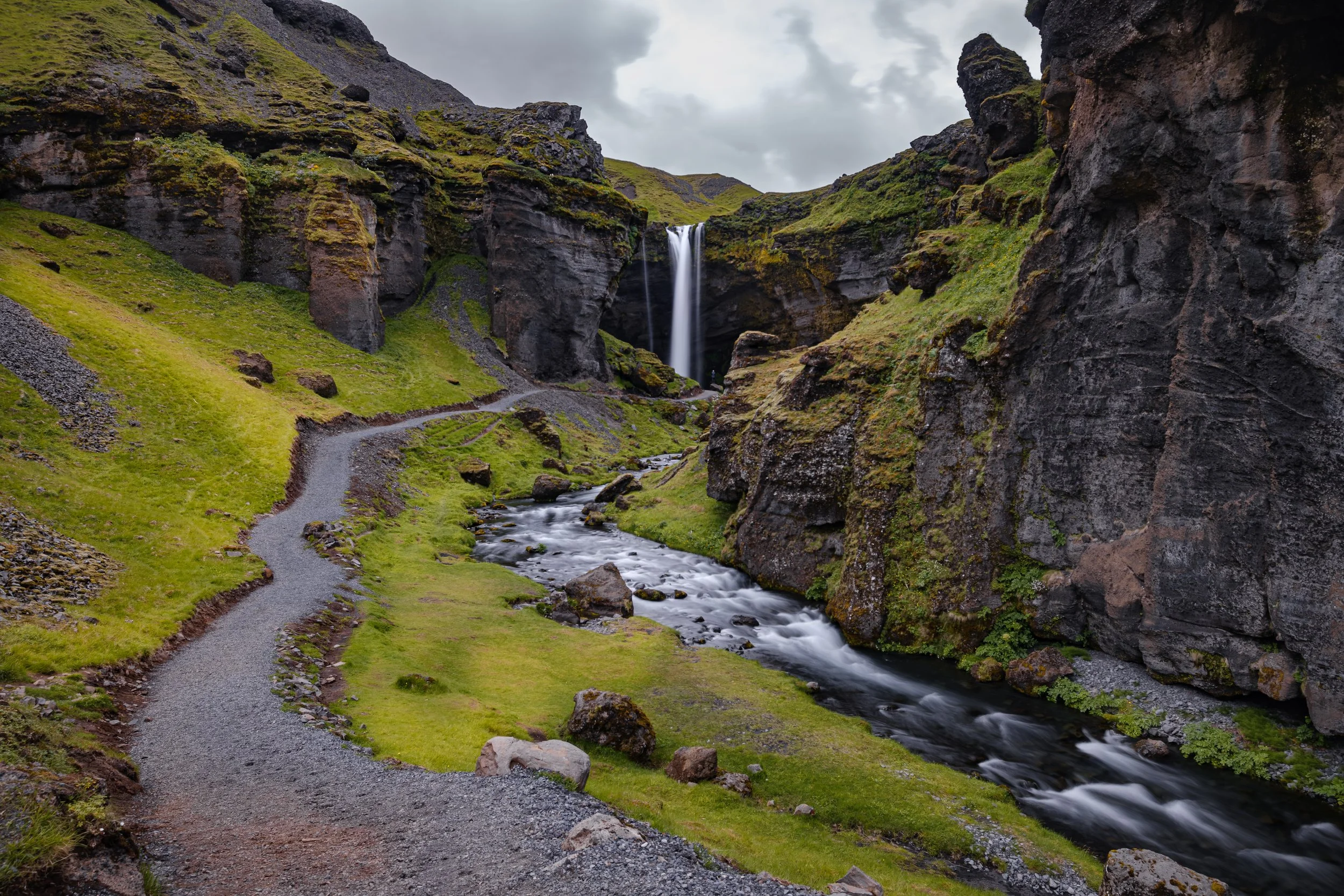 Cascata Kvernufoss entre falésias verdes no sul da Islândia, com um trilho junto ao rio.