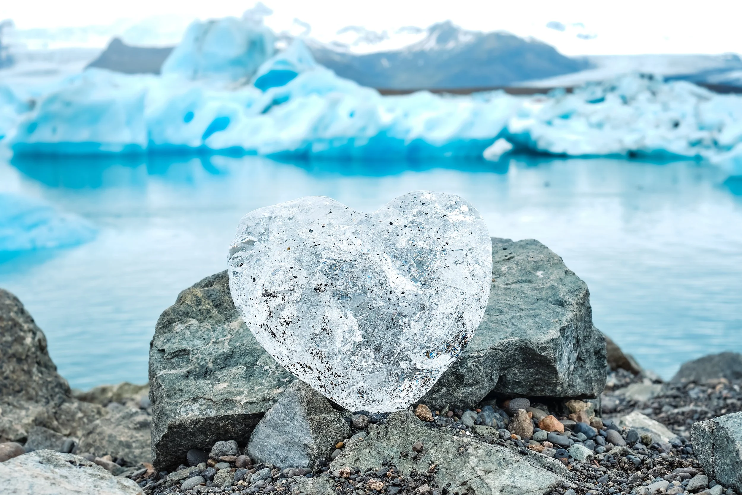 Coração de gelo sobre as rochas junto à lagoa glaciar Jökulsárlón, com icebergs ao fundo na Islândia.