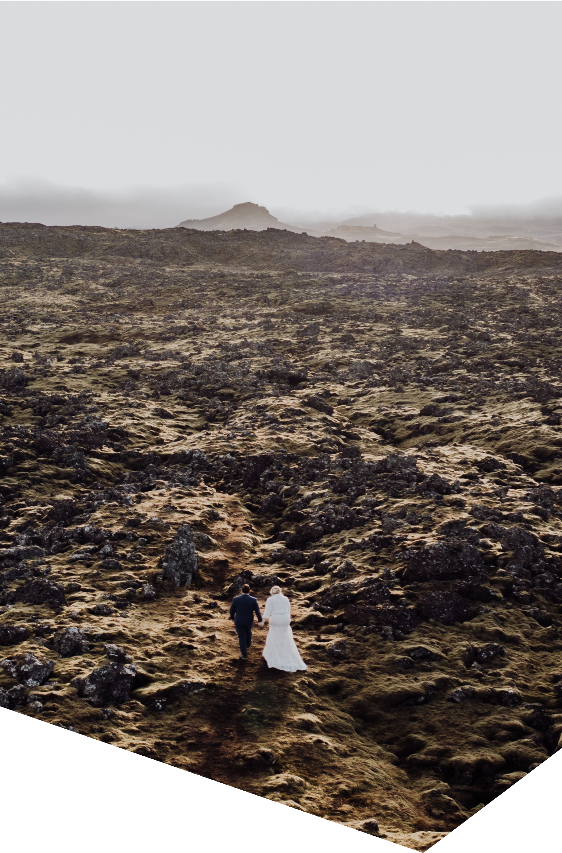 Casal em traje de casamento a caminhar por uma paisagem vulcânica em Vík, Islândia.