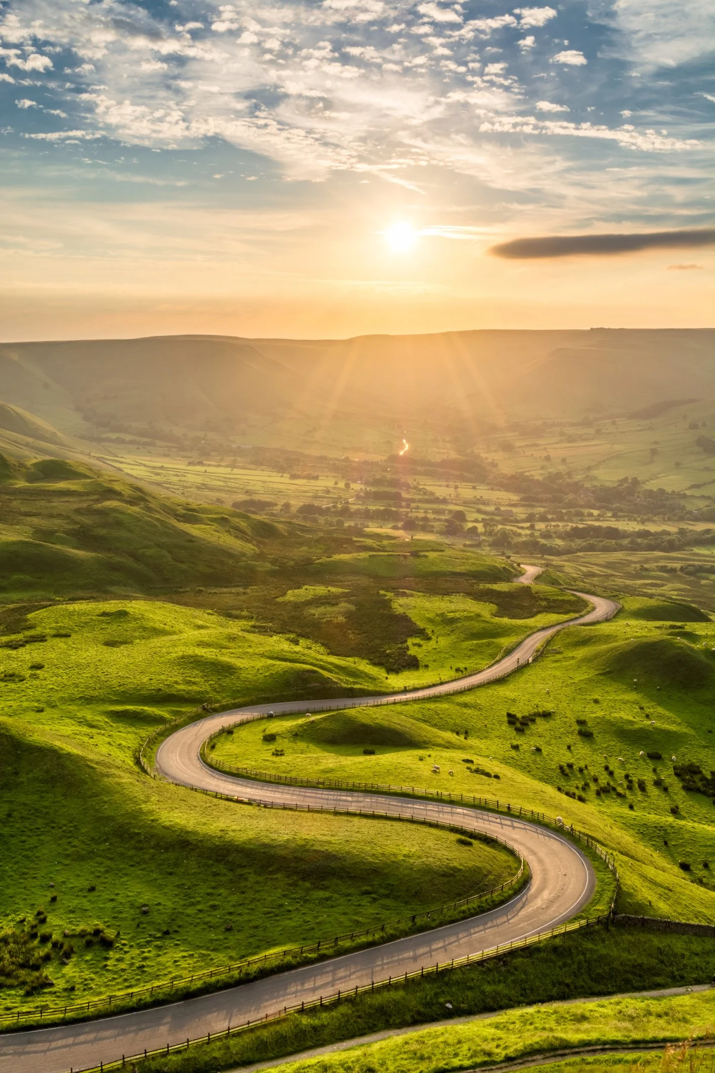 A winding road through green rolling hills at sunset.