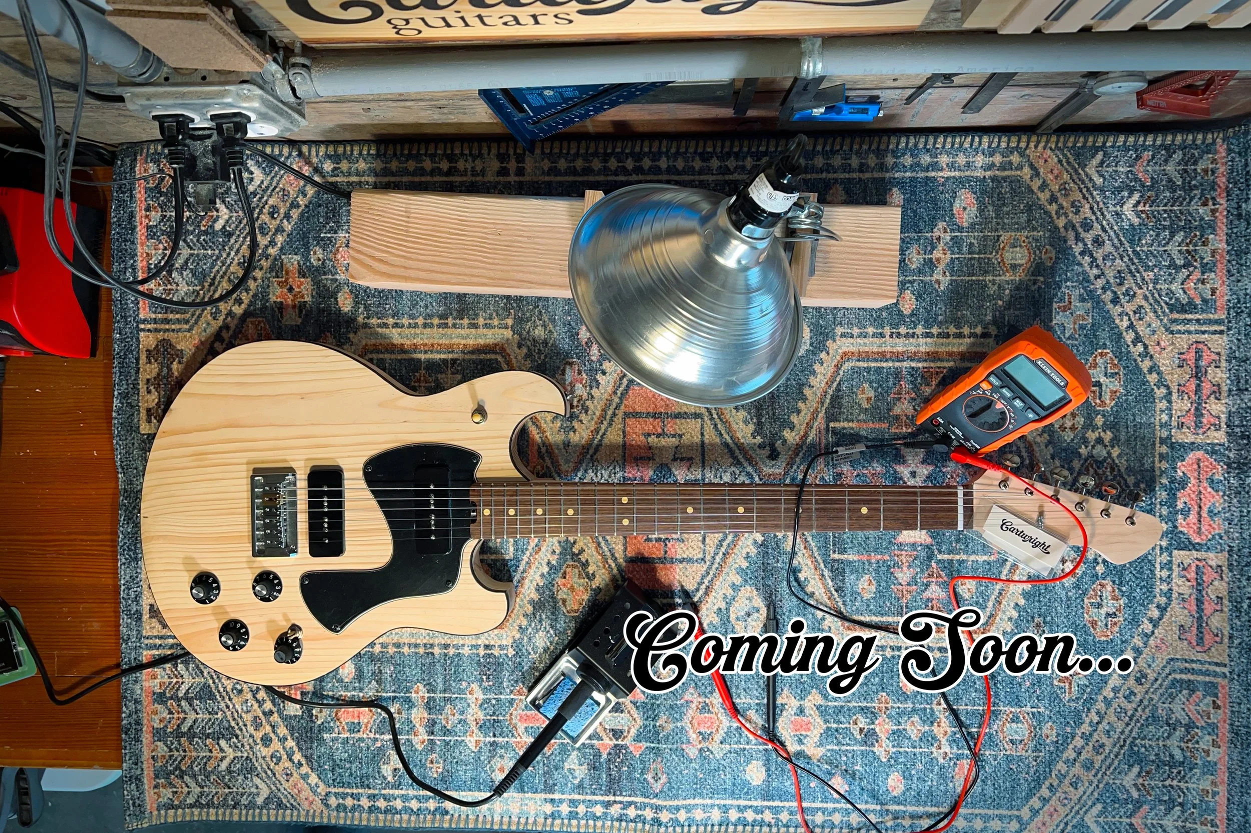 Partially completed guitar sitting on workbench with the words "Coming Soon" overlayed on it.