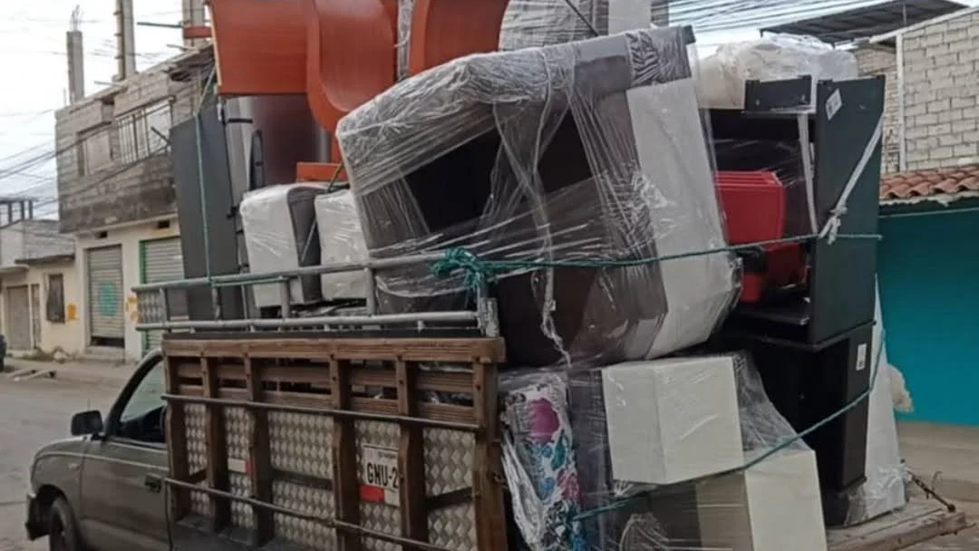 Camioneta cargada con electrodomésticos y muebles envueltos en plástico y amarrados con cuerdas en una calle de una zona residencial.