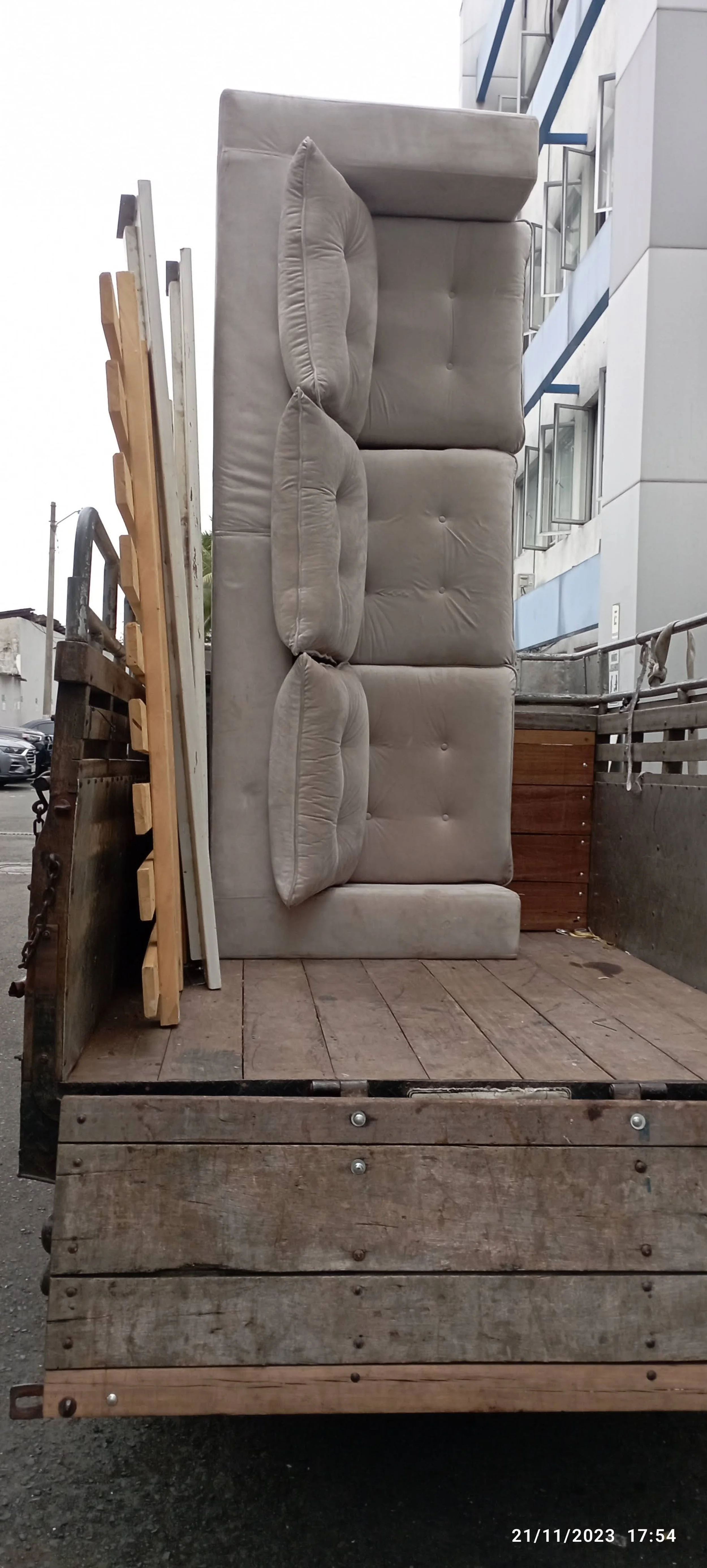 Furgoneta con respaldo de muebles, incluyendo sillones y tablas de madera, en un área urbana.