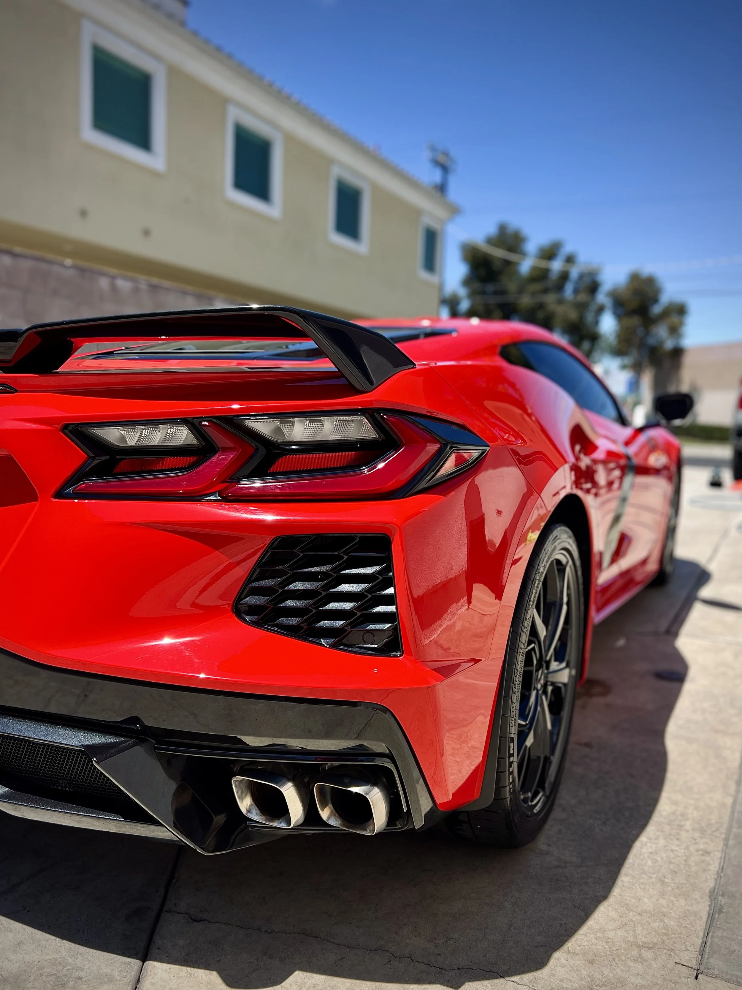 Red sports car parked on a driveway with a yellow house and blue sky in the background.