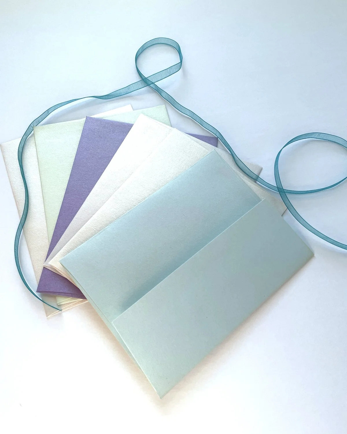 A collection of pastel-colored paper cards fanned out on a white surface, with a blue ribbon loosely draped over them.