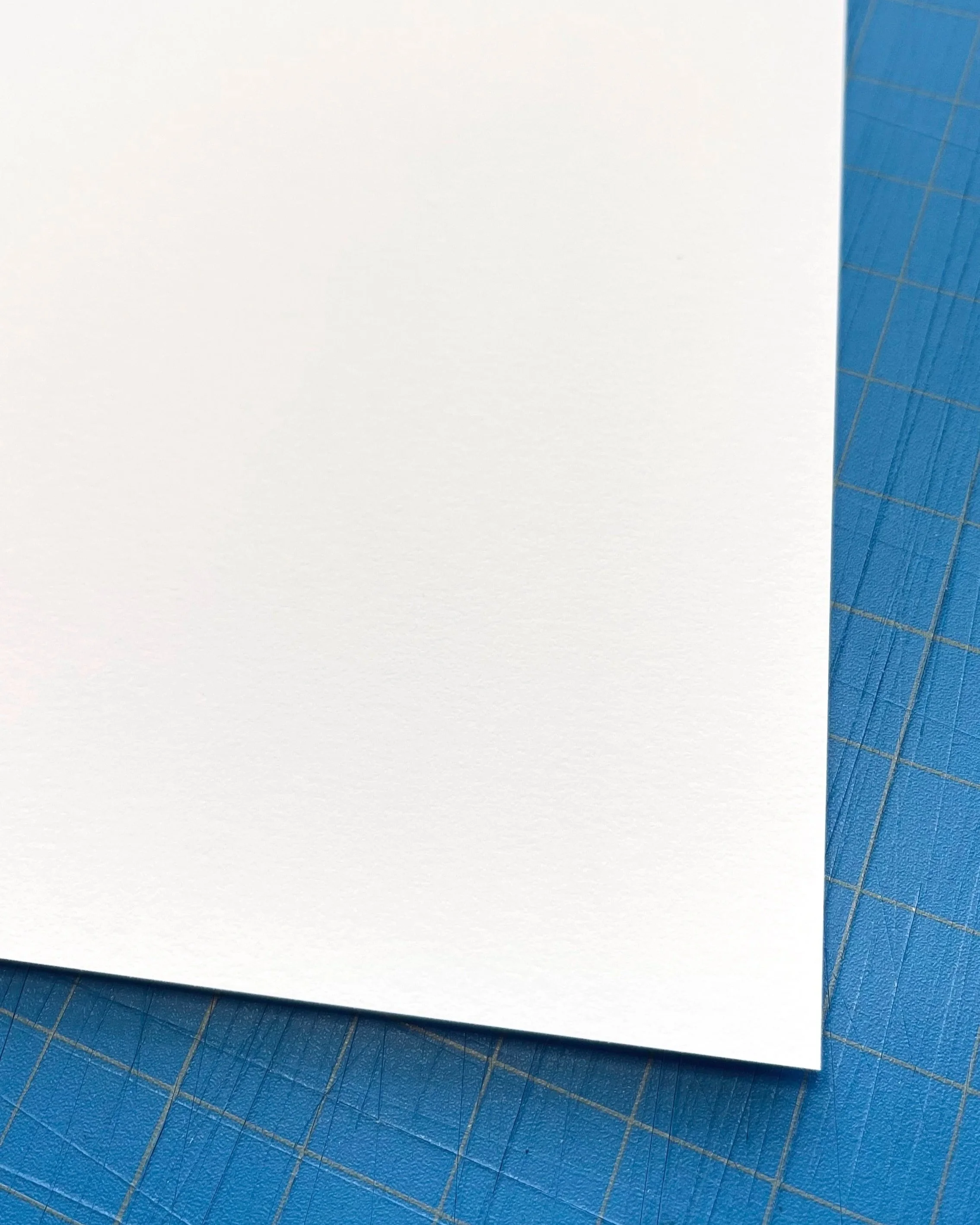 Close-up of a blank white piece of paper on a blue cutting mat with grid lines.