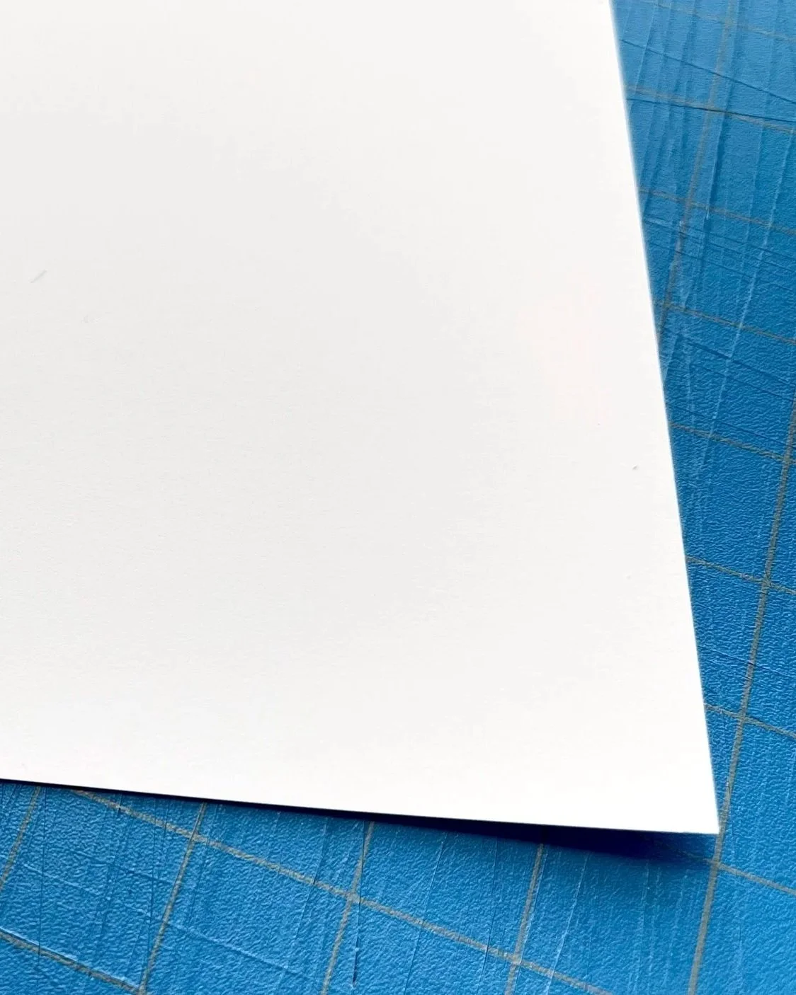 Close-up of a white sheet of paper on a blue cutting mat with grid lines.