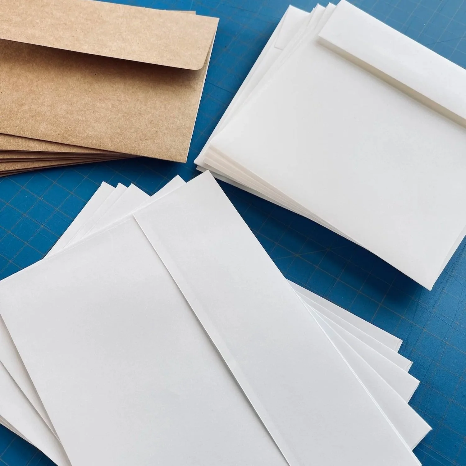 Brown paper envelopes and white sheets of paper on a blue cutting mat.