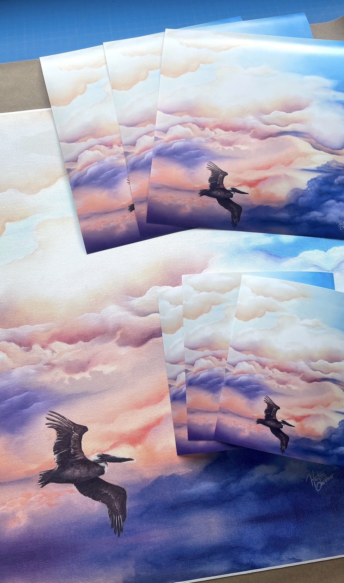 Multiple prints or canvas art pieces depicting a bird flying across a colorful sky with clouds, some with pink and orange hues, others with purple and blue tones.
