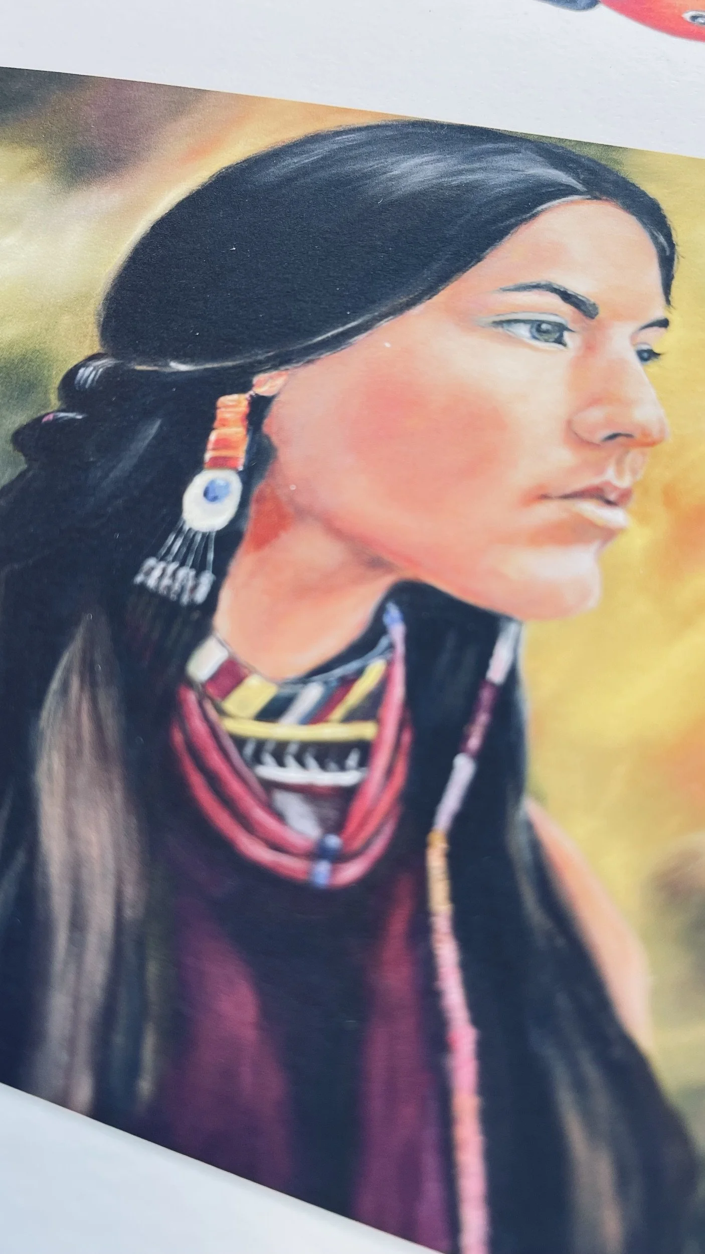 Close-up of a fine art print on heavyweight, natural cotton rag paper. A colorful painting of a Native American woman with black hair, wearing traditional jewelry and clothing, gazing to the right.