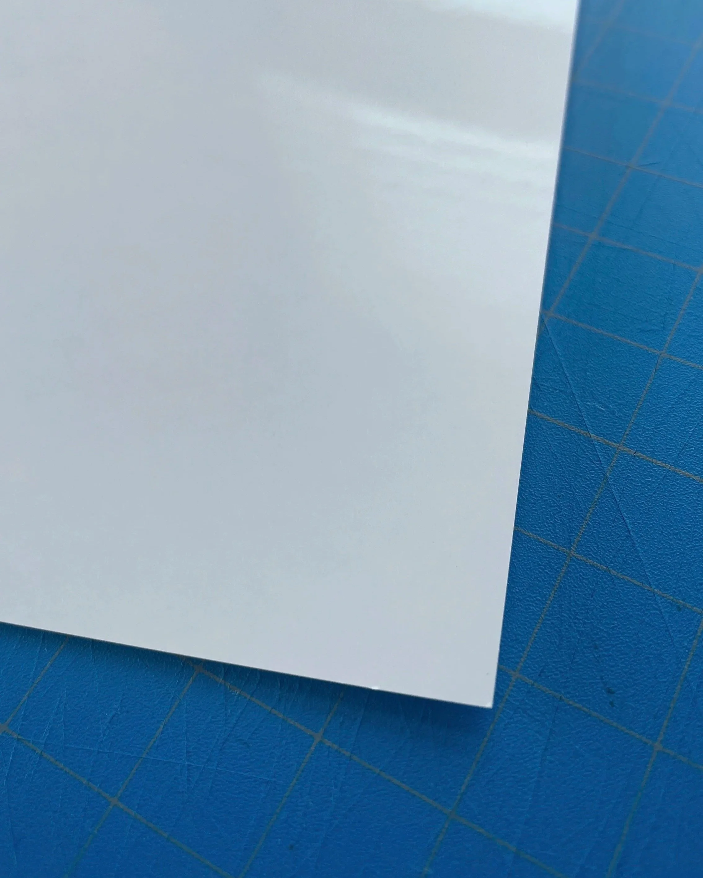Close-up of a white sheet of paper on a blue cutting mat with grid lines.