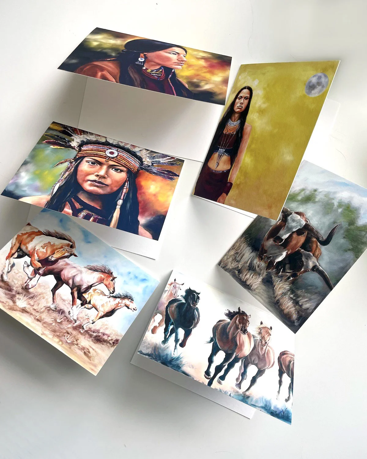 Collection of seven colorful paintings depicting Native American women in traditional attire, horses running through fields, and a person standing under a moonlit sky.