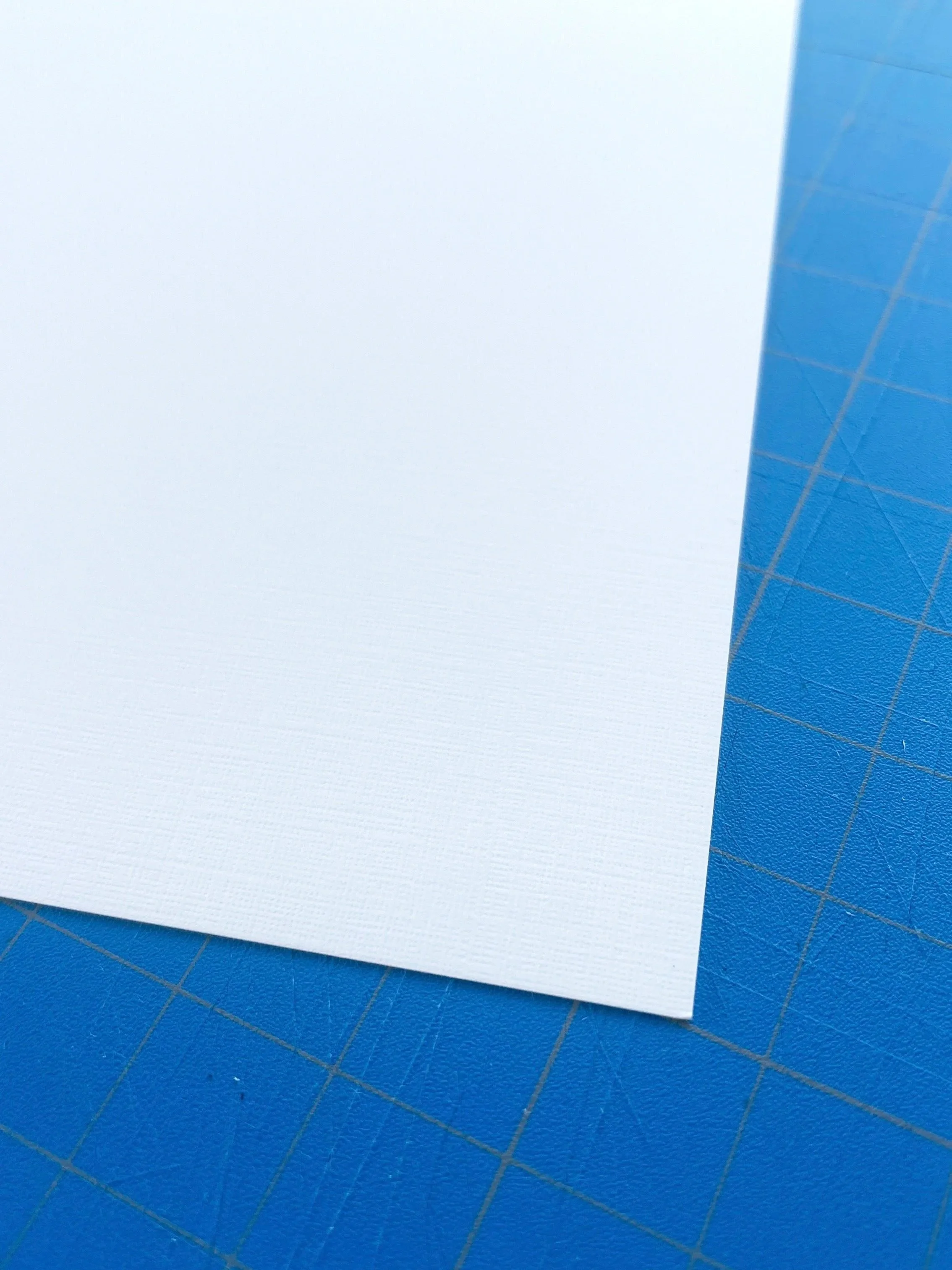 Close-up of a blank white textured sheet of paper on a blue cutting mat with grid lines.