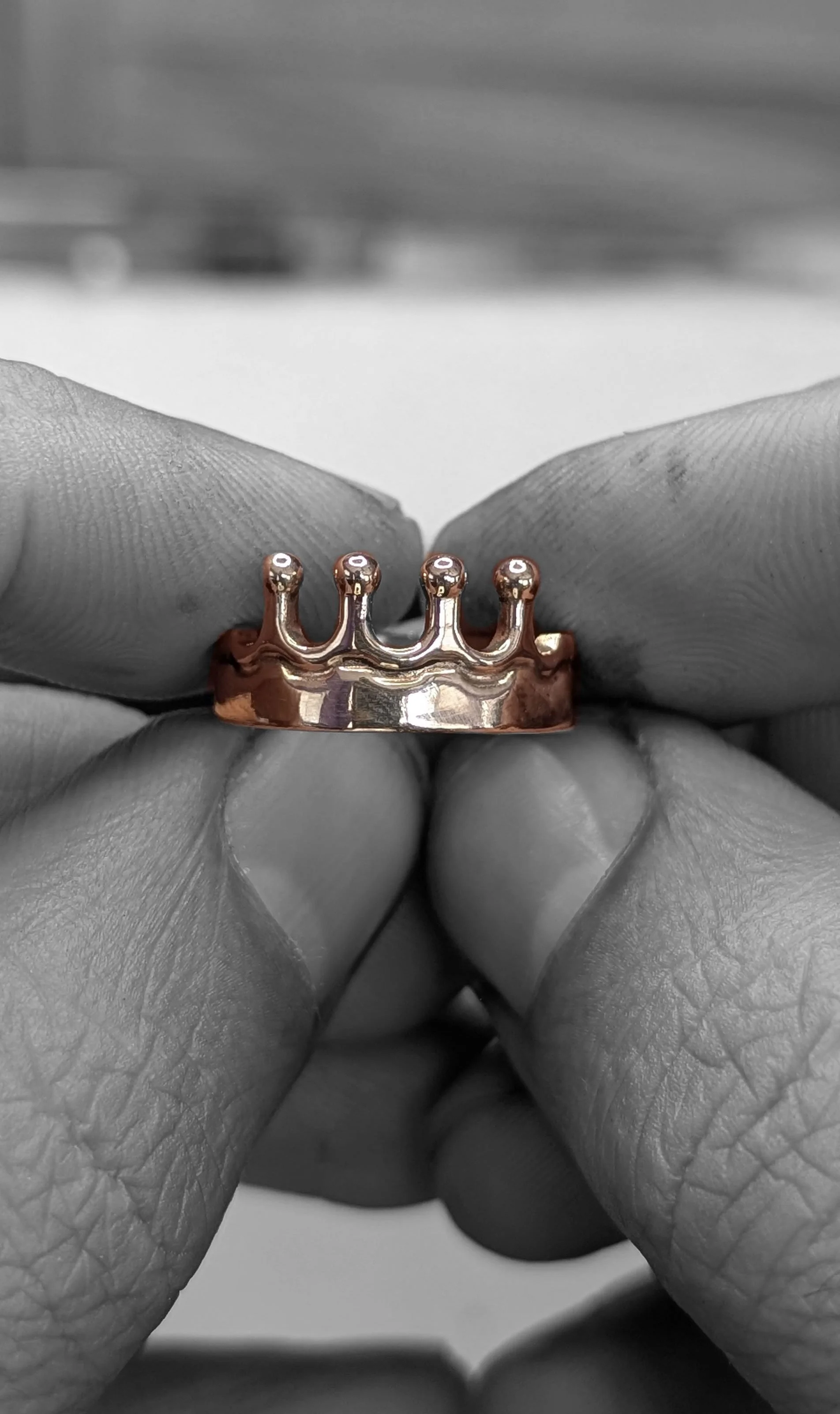 Close-up of a person's hand holding a small copper-colored crown-shaped ring, black-and-white filter.