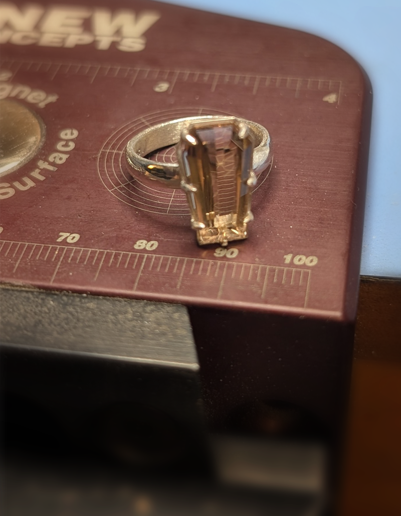 Silver ring with a large rectangular citrine, in a prong setting, placed on a metal surface with a ruler for scale.
