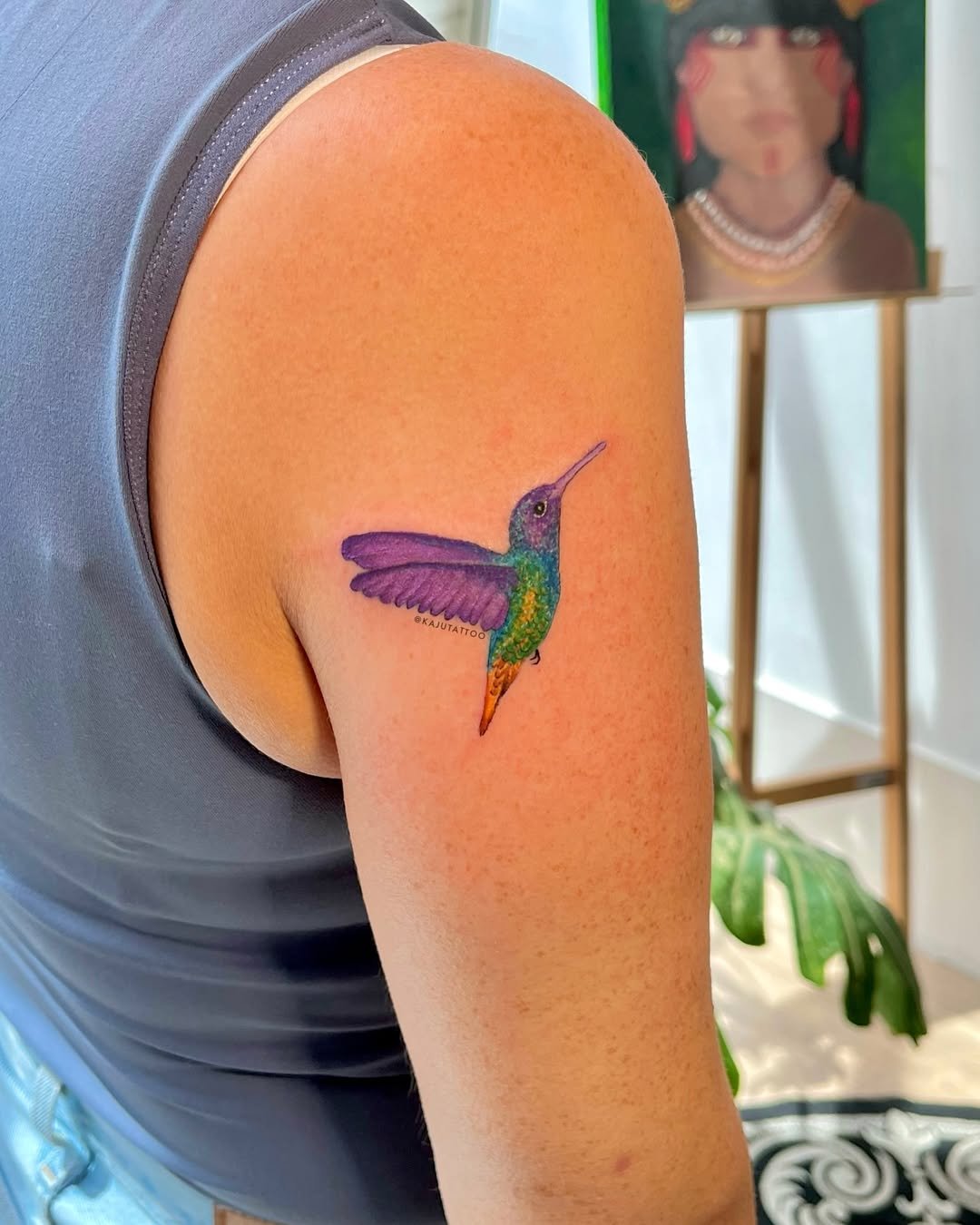 Tatuagem de beija-flor colorido na parte superior do braço de uma pessoa.