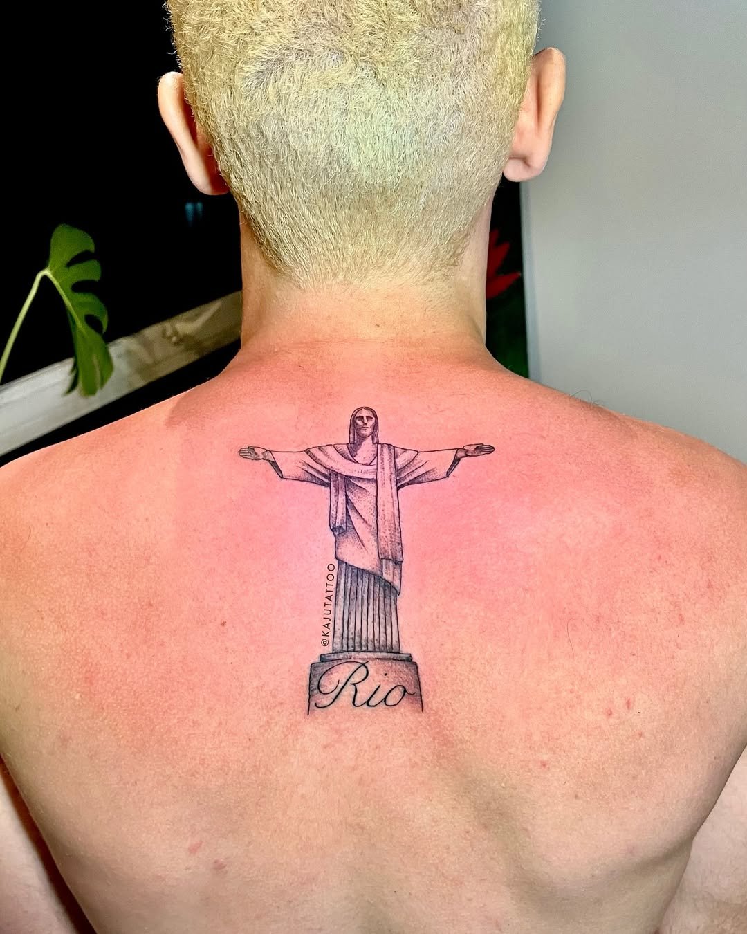 Tatuagem da estátua do Cristo Redentor com as mãos abertas e a palavra "Rio" abaixo na parte superior das costas do homem