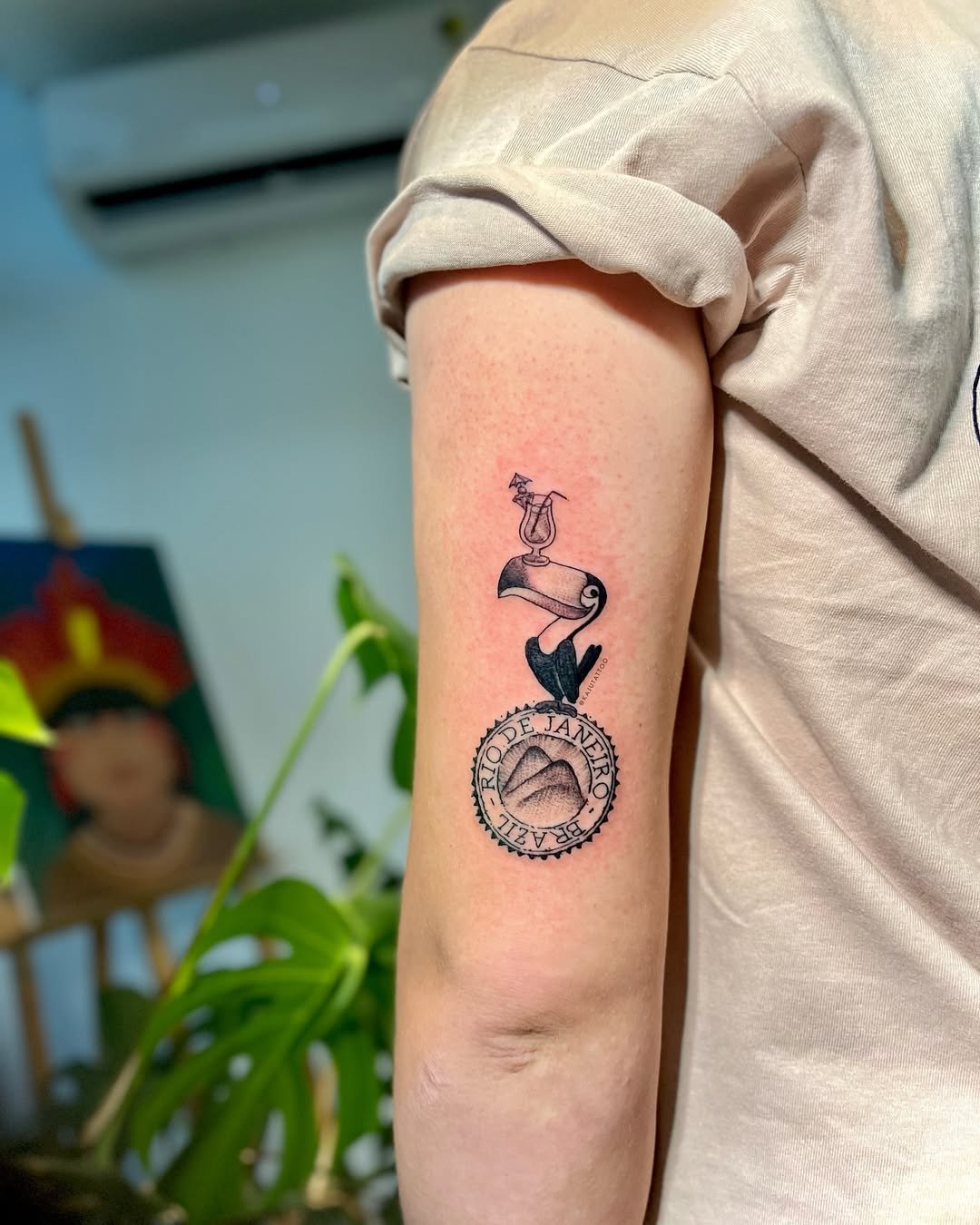 Tattoo no braço de uma pessoa representando o Rio de Janeiro, com uma garrafa de cerveja vazia, um passarinho e uma montanha estilizada, com a inscrição "RIO DE JANEIRO" ao redor.