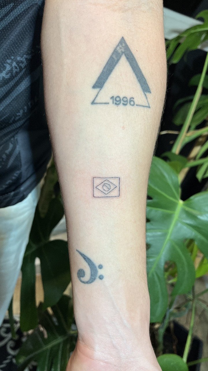 Tatuagens no antebraço com símbolos e o ano 1996.