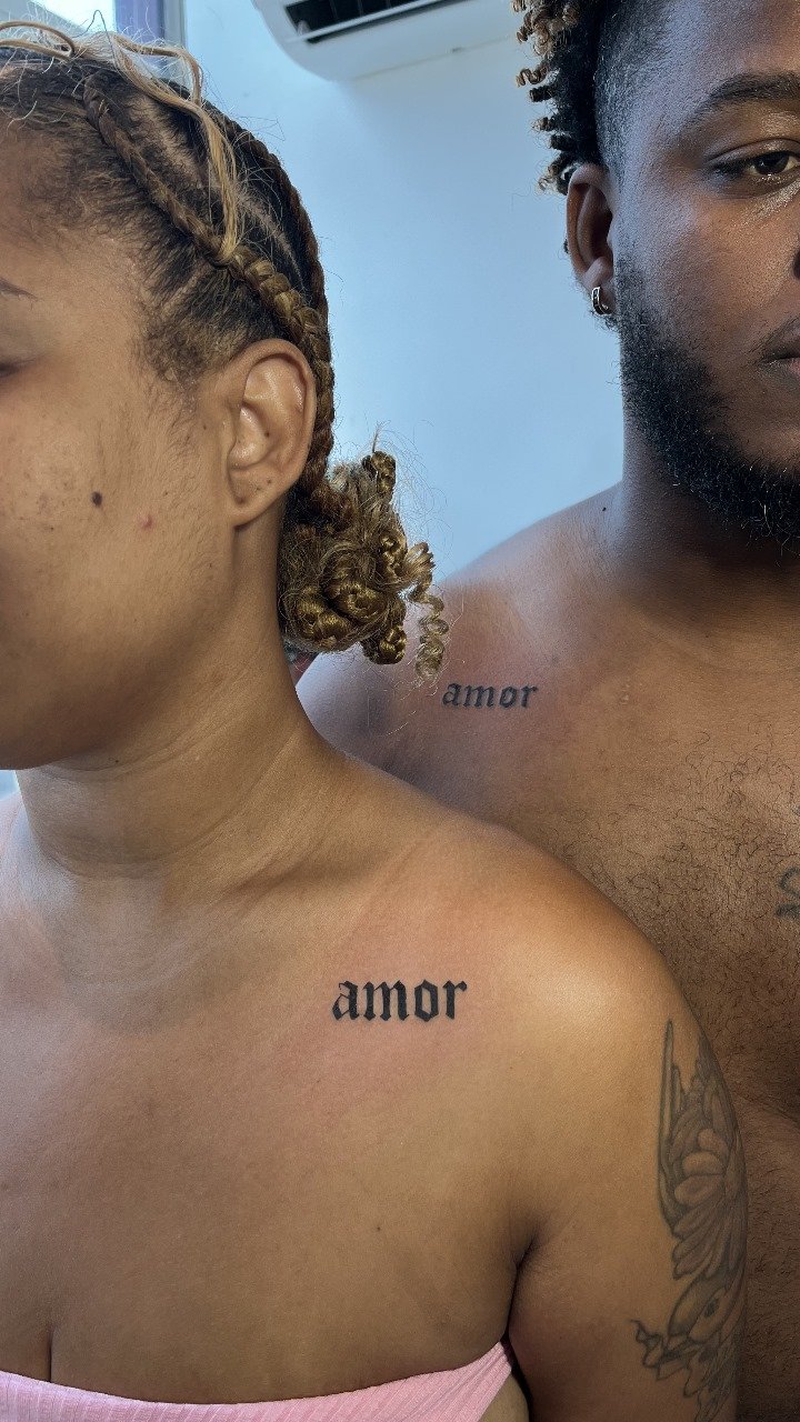 Imagem de duas pessoas com tatuagens na altura do ombro que dizem 'amor'.