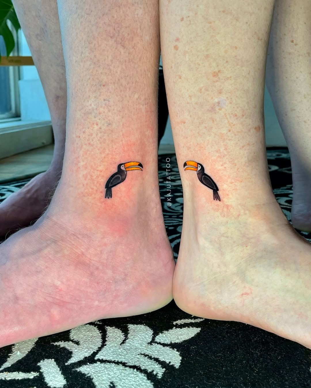 Tattoos de tucano preto e laranja nas laterais dos tornozelos.