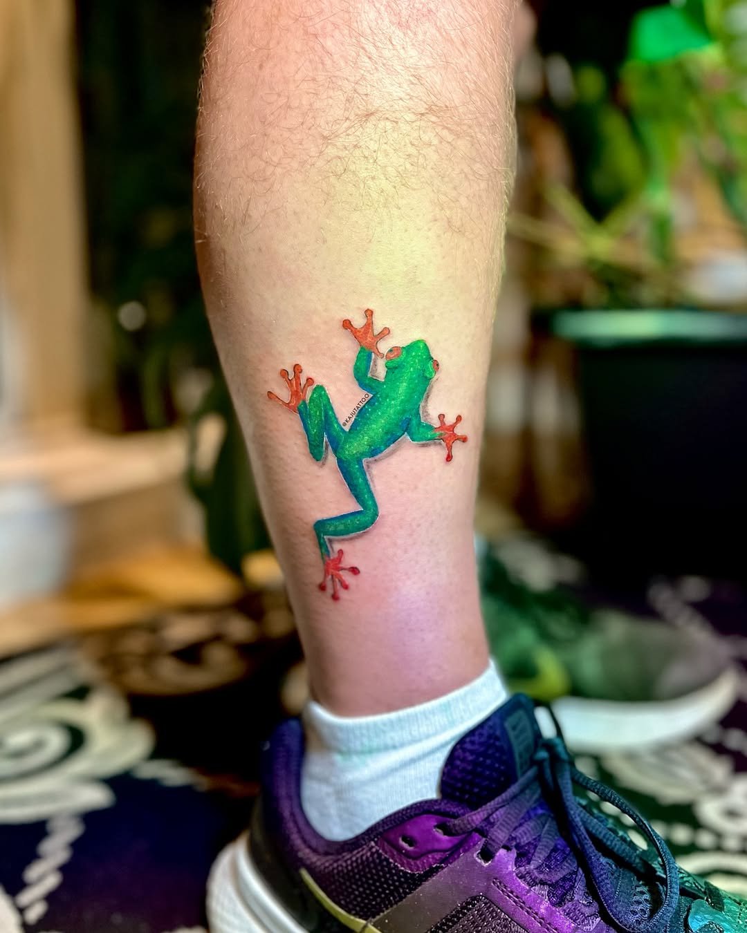 Tattoo de uma rã colorida na perna de uma pessoa