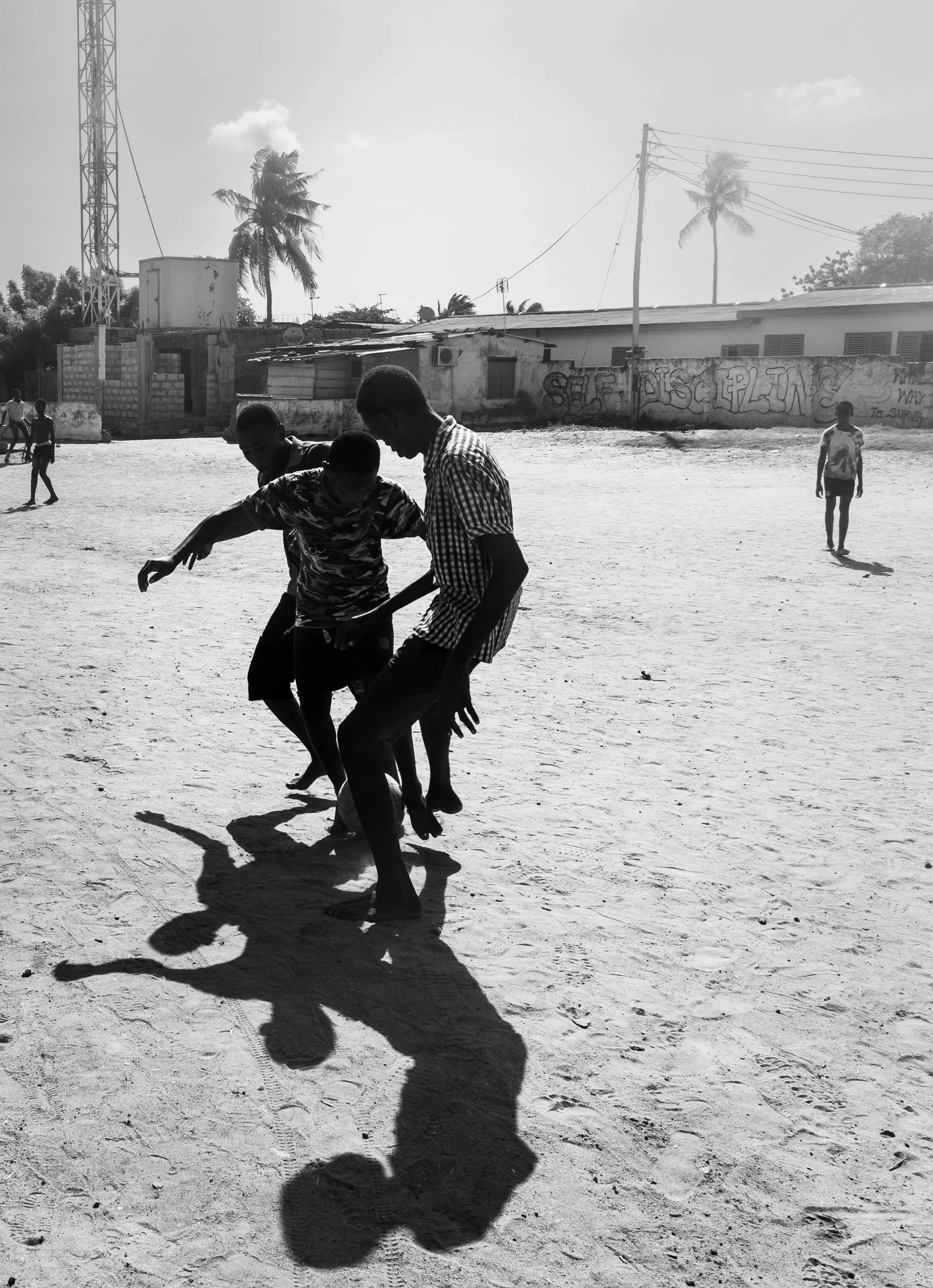 Under the mid-day sun, kids playing football in a dirt lot in Teshie, Ghana.
