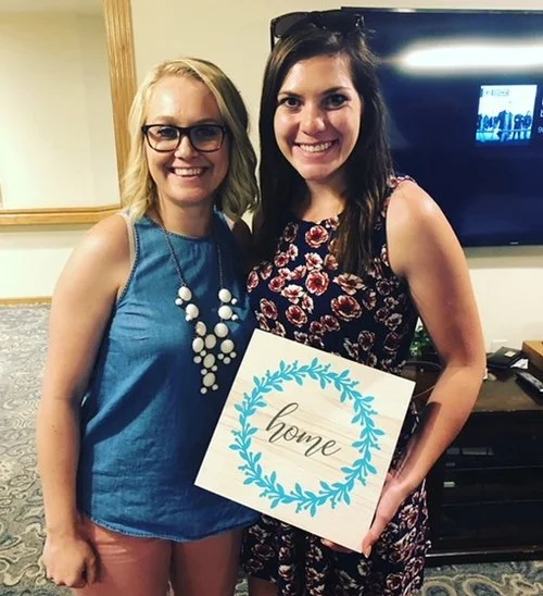 Two women smiling indoors, one holding a 