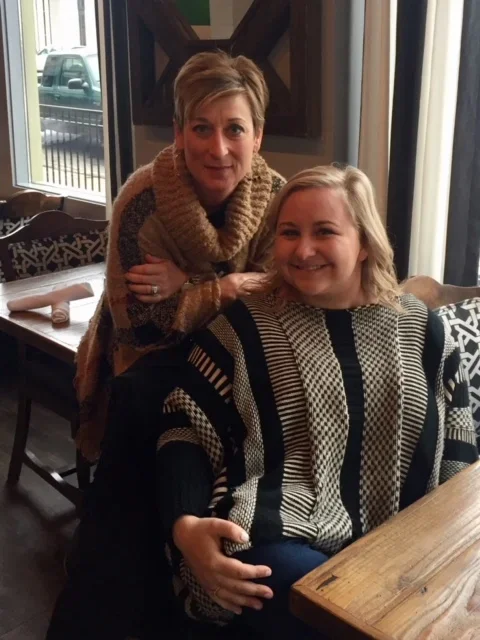 A woman and a girl seated at a wooden table in a restaurant, smiling at the camera.
