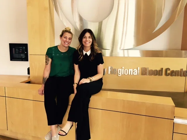 Two women smiling and sitting on a wooden counter at the Regional Blood Center.