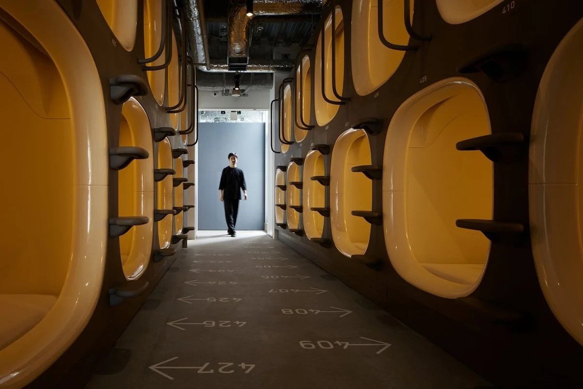 Modern capsule hotel hallway at 9h Nine Hours Akasaka, Tokyo. Features futuristic yellow sleeping pods and a minimalist interior for solo travelers.
