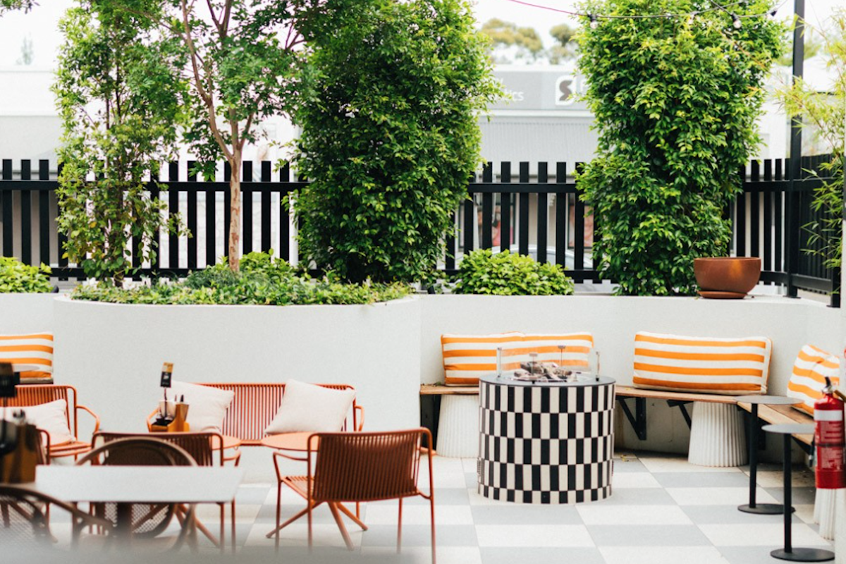 Outdoor beer garden at Sussex Hotel featuring a black and white tiled fire pit table, orange striped cushions, and lush green plants.