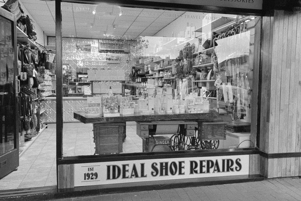 Exterior of Ideal Shoe Repairs storefront, established in 1929, showing a window display of leather care products and vintage sewing machine tables.