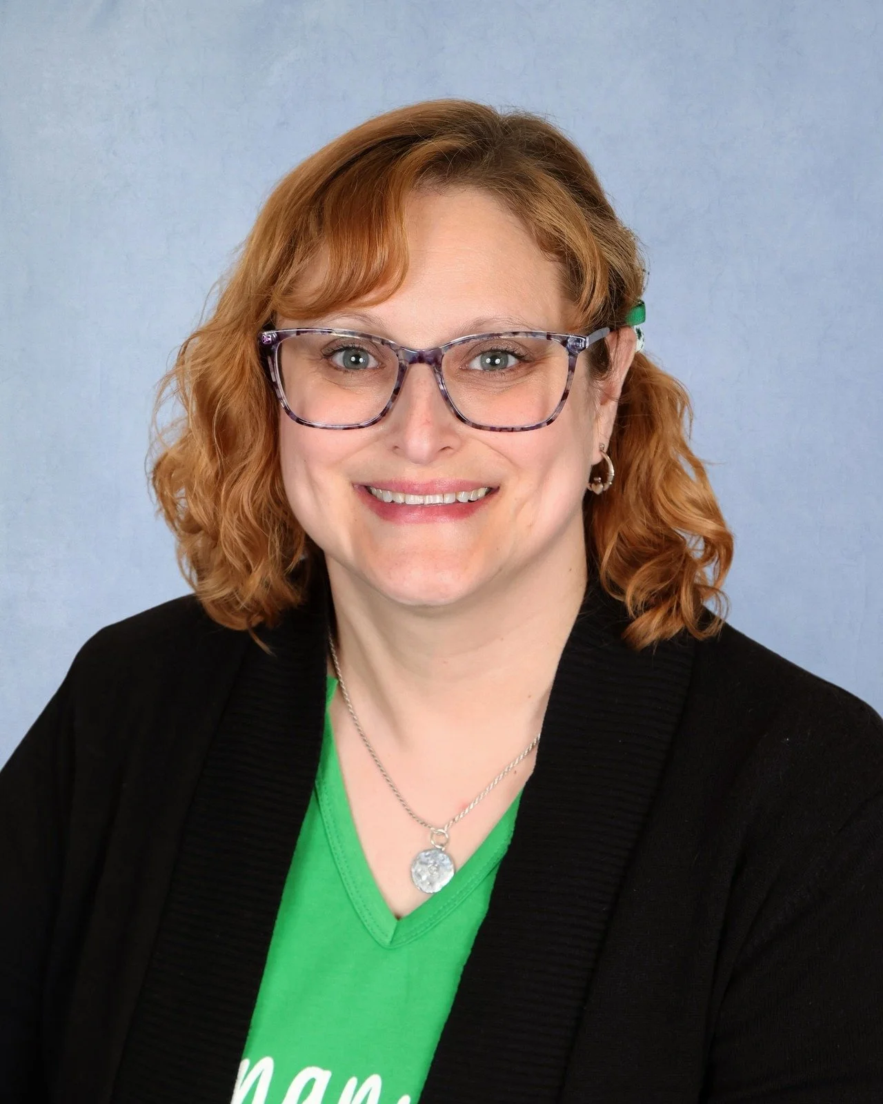 A woman with wavy red hair smiling in front of a light blue background.