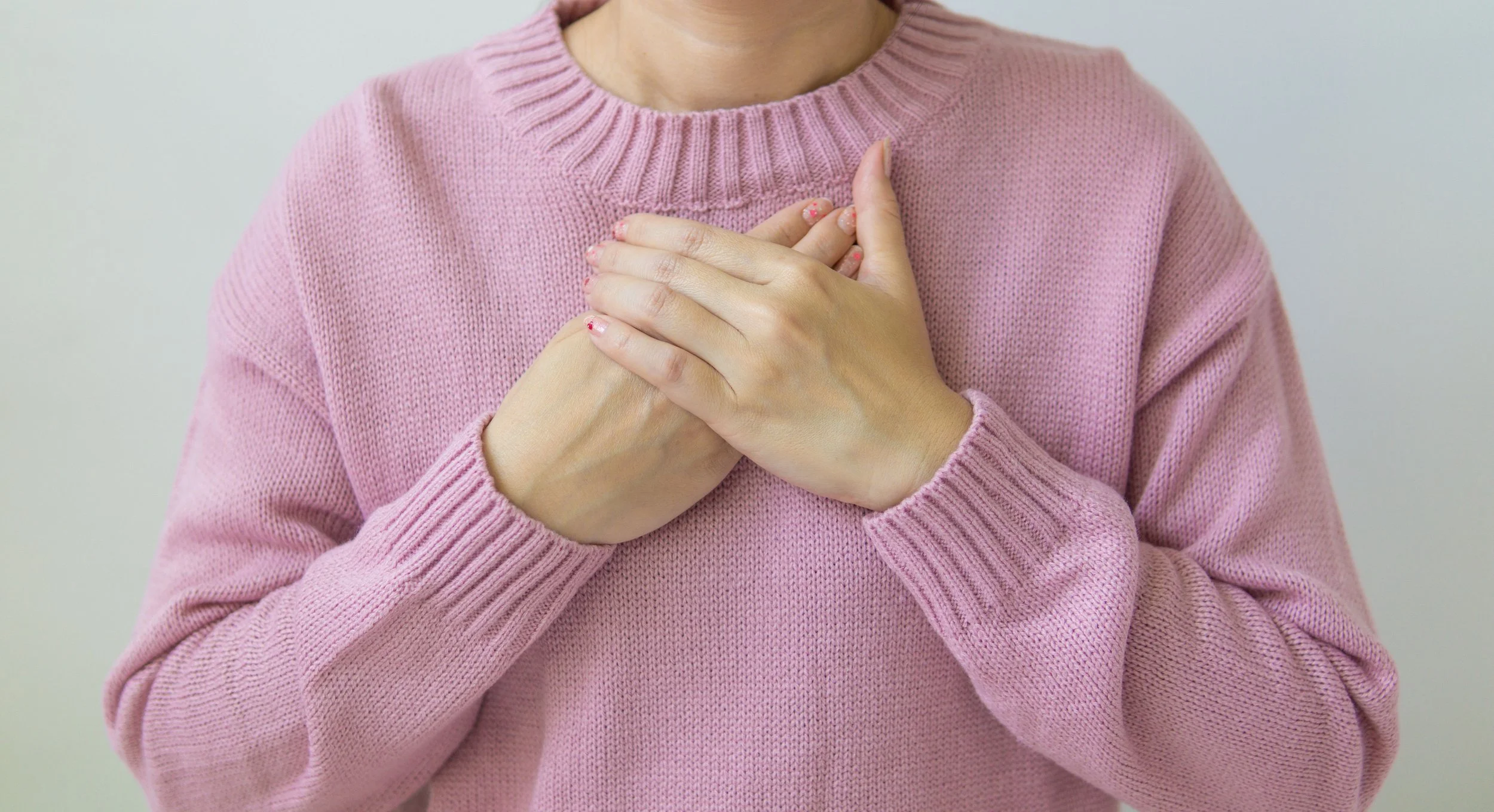 Person wearing a pink sweater with hands crossed over heart.