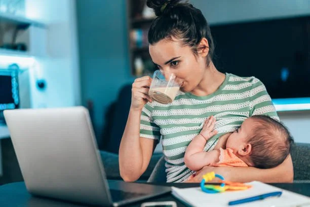A young woman breastfeeding a baby while working on a laptop. The Whole Parent Collective support working parents.