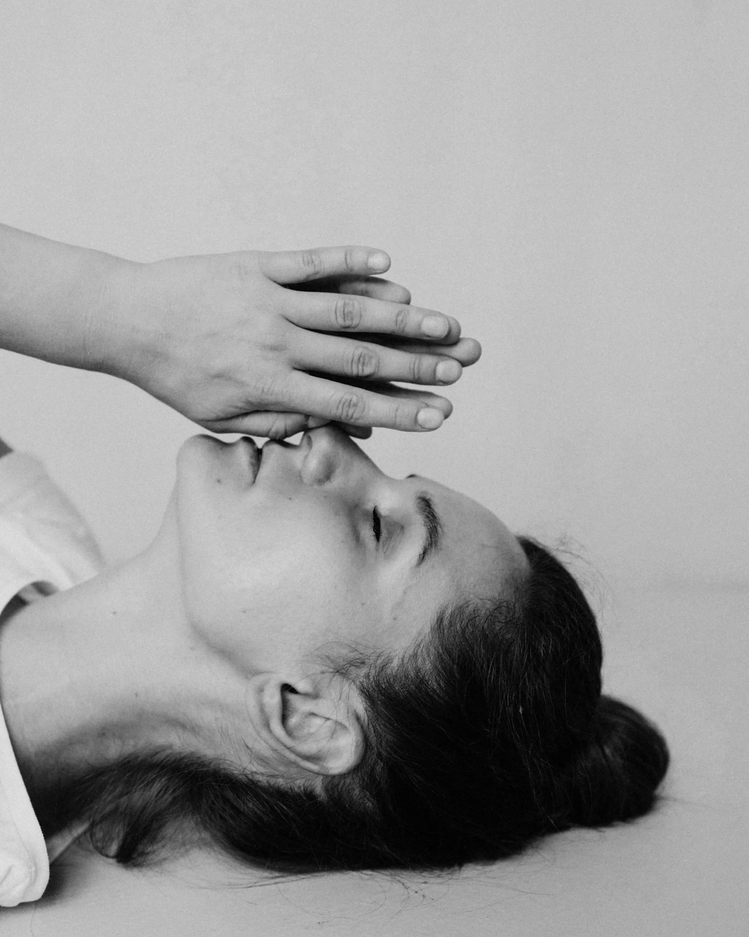 A person resting on a flat surface with their eyes closed and hands gently resting on their mouth