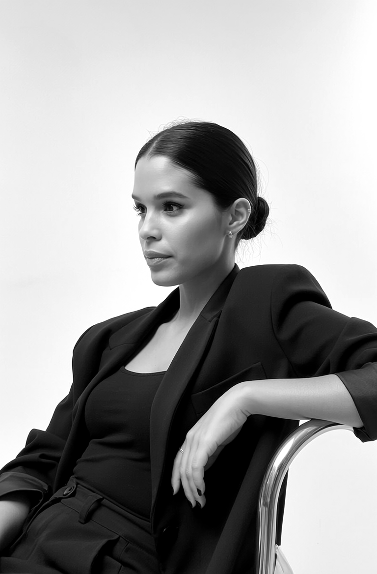 Retrato en blanco y negro de una mujer con traje negro sentada en una silla, mirando de perfil.