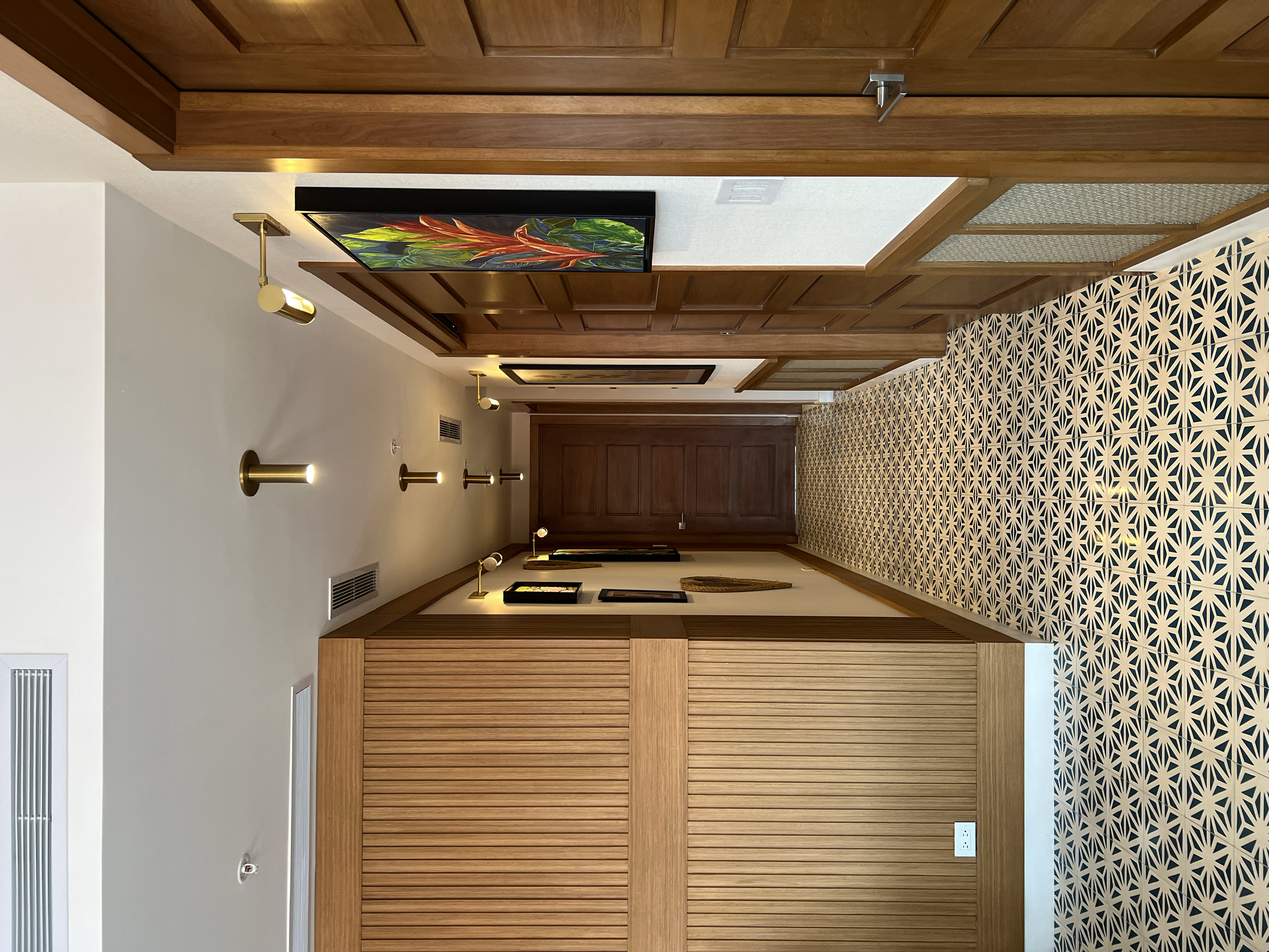 Pasillo con paredes de madera y piso de baldosas con patrón floral, decorado con cuadros y una pintura colorida, iluminación moderna en el techo.