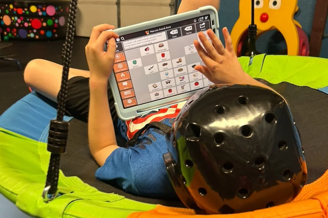 Child wearing a helmet lying on a trampoline and using a tablet with a food and drink app.