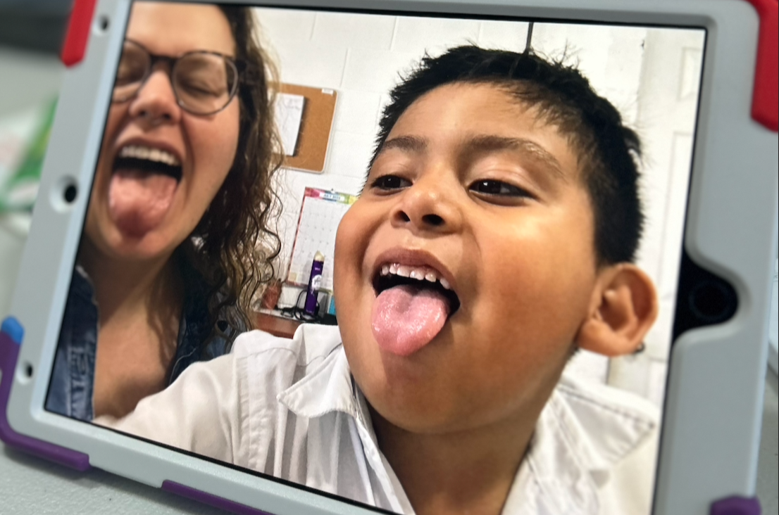 A young boy and an adult woman are taking a selfie together, both sticking out their tongues and making silly faces.